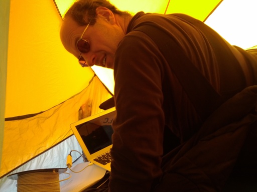 Craig working on his laptop computer in his tent, connected by a 50 metre spool of cable to PLATO-R. CREDIT: Luke Bycroft. (click to enlarge)